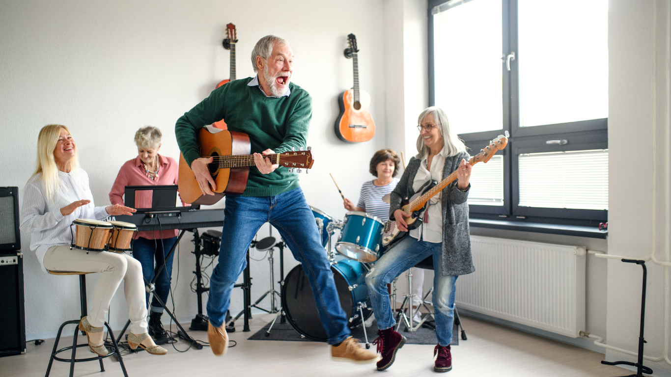 A senior guitarist jumping for joy as his band continues in the background
