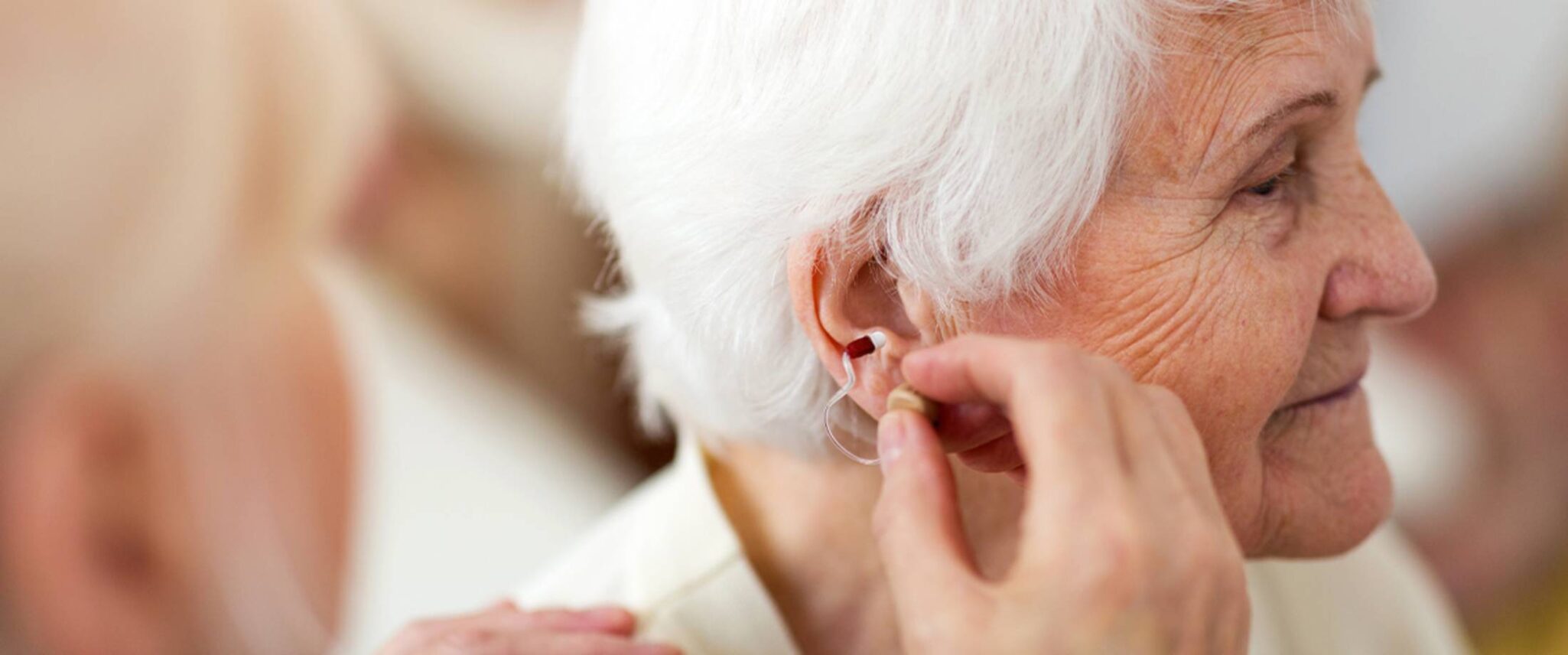 woman helping an elderly woman put in a hearing aid