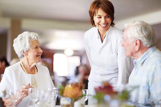 A waitress chats with a senior couple at a formal dining table.