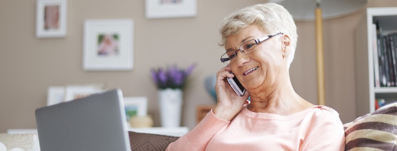 Happy senior woman talking on her phone while using a laptop