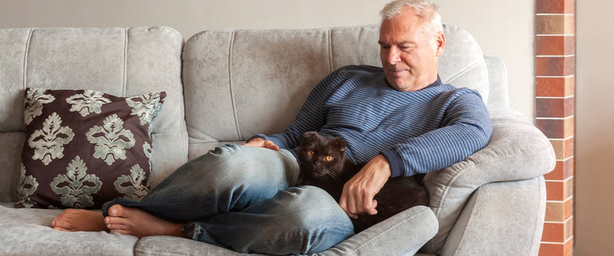 senior man cuddles his cat on the couch of his senior living apartment