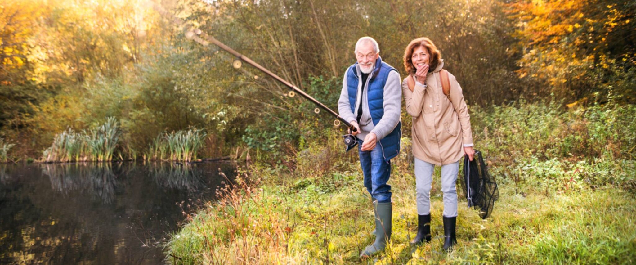 A senior couple going fishing amid a scenic wooded area.