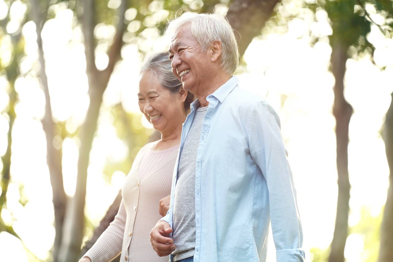 A woman and a man go walking on a tree-shaded path hand in hand