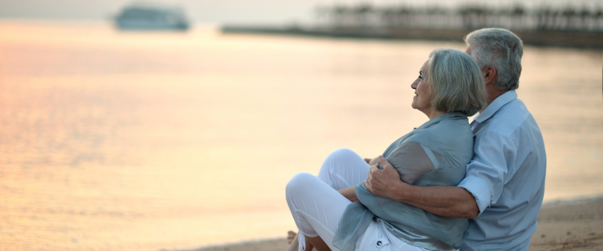 older couple cuddled on a beach at sunset