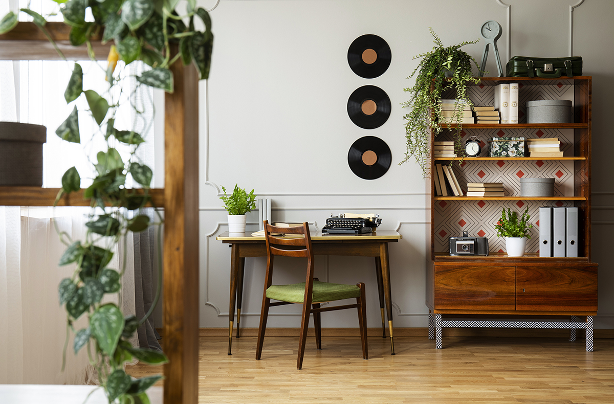 Black retro typewriter on a unique wooden desk, a mid-century modern chair and a renovated bookcase in a hipster home office interior