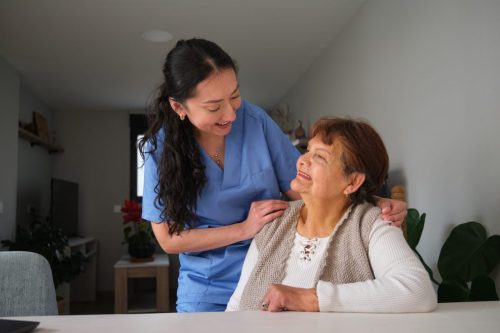 Young nurse comforting elderly woman at home